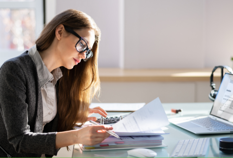 Femme assise devant un bureau avec des documents et un ordinateur symbolisant la facturation électronique des associations.